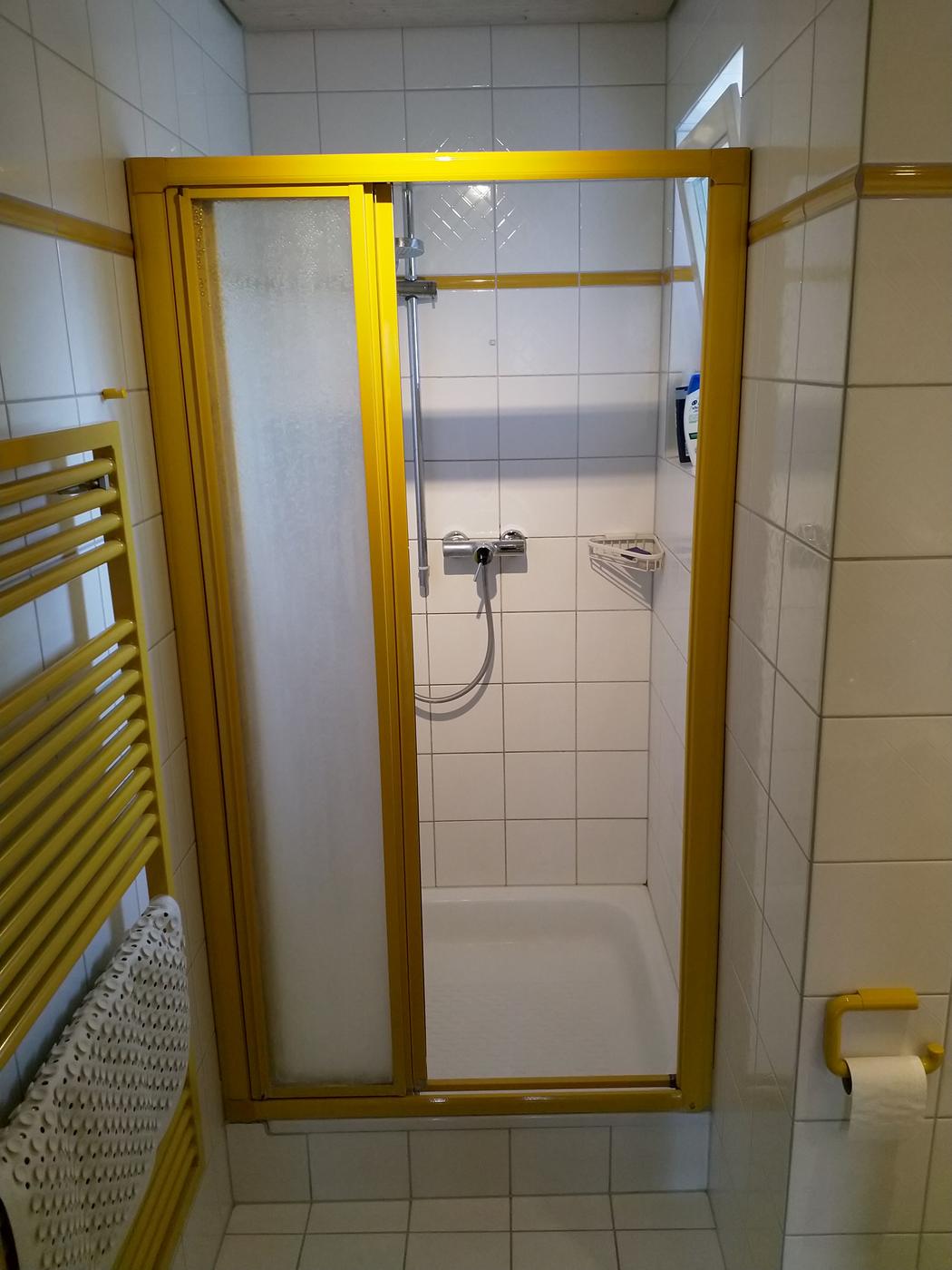 Vorher: Dusche mit weißen Fliesen und gelbem Rahmen
